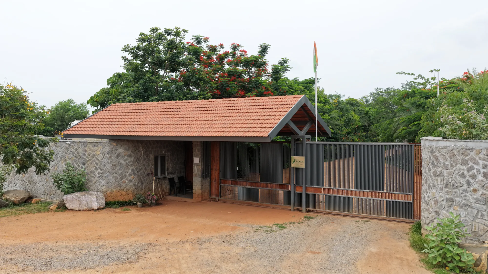 Entrance gatehouse with a tiled roof and stone walls at Woods Shamshabad, Hyderabad